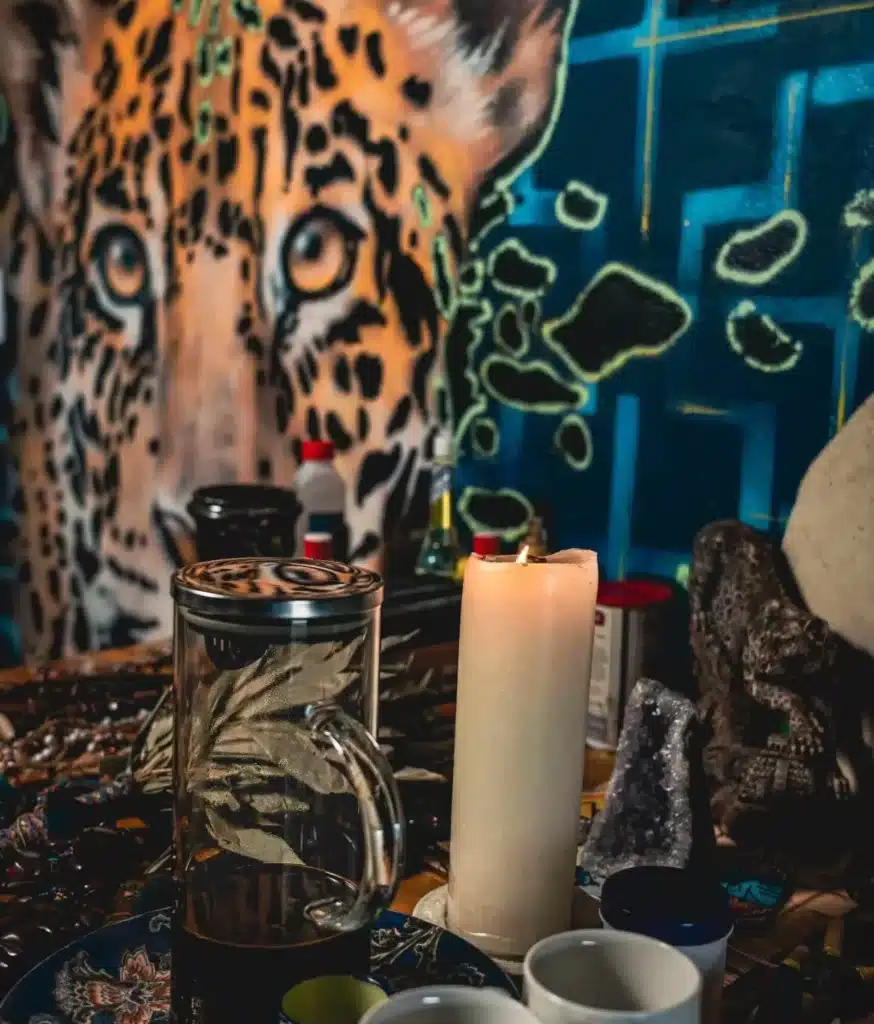 harmonica retreat altar with the Ayahuasca, the cups, a lit candle, ornaments decorating the alter. And artwork in the background of the jungle, featuring the jaguar.