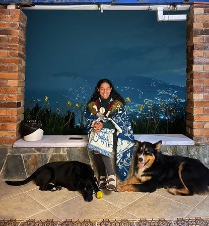 Jenna from Harmonica Retreat sitting at the retreat center with the two dogs next to her and the mountains and lights in the background