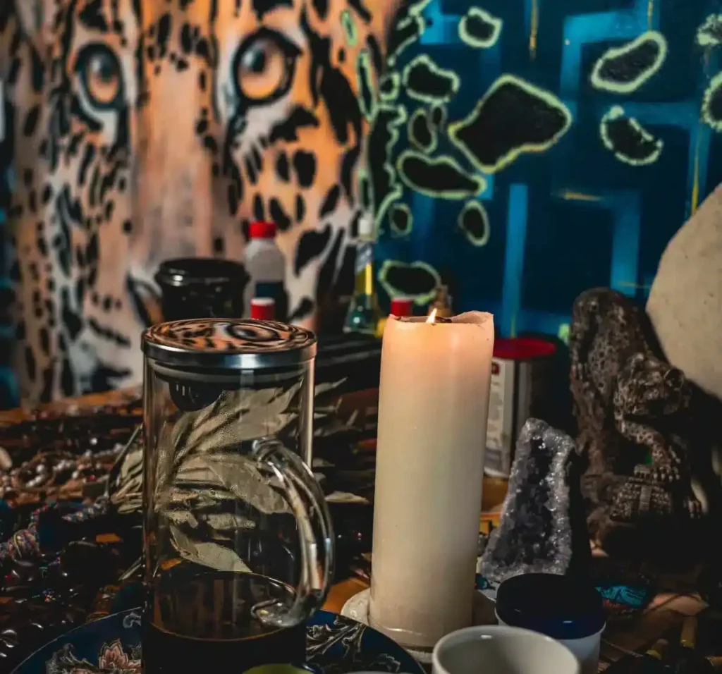 harmonica retreat altar with the Ayahuasca, the cups, a lit candle, ornaments decorating the alter. And artwork in the background of the jungle, featuring the jaguar