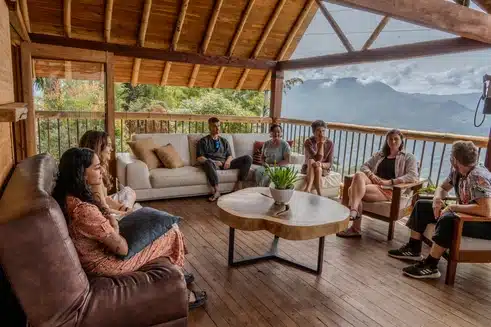 A group of people sat around the table talking in a sharing circle at their ayahuasca retreat. With the team and other participants