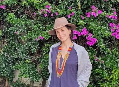 female therapist in purple shirt smiling with pink flowers and bushes in the background