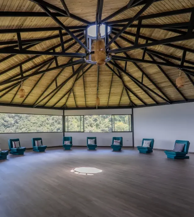 The maloka ceremony space at Harmonica Retreat, with teal chairs arranged in a circle beneath the wooden roof and the Colombian mountains through the windows