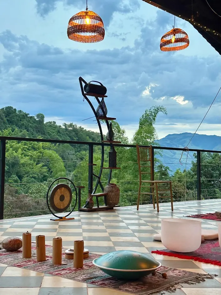 Sound bath instruments set out on the terrace at Harmonica Retreat: a gong, handpan, bamboo chimes and crystal bowls, with the valley and mountains behind