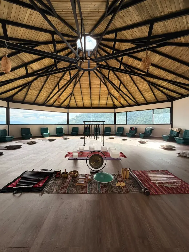 The maloka at Harmonica Retreat set up for a sound healing ceremony: crystal bowls, a gong, chimes and tuning forks laid out on rugs in the centre of the round hall, seats around the edge and the mountains through the windows
