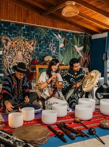 Sergio, Vanessa and Kevin playing singing bowls and a frame drum at a sound healing ceremony in front of the jaguar mural at Harmonica Retreat