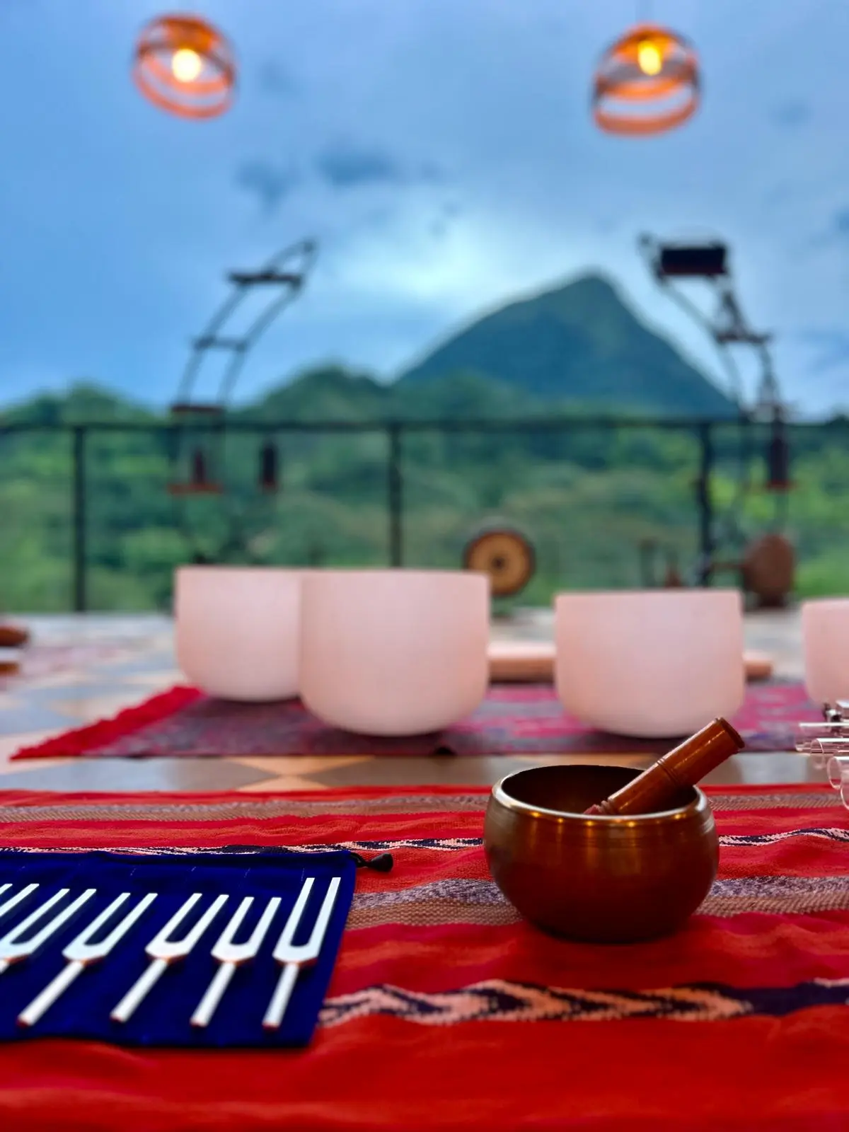 Tuning forks and a brass singing bowl in the foreground of a sound healing setup, crystal bowls and Cerro Tusa in the background at dusk