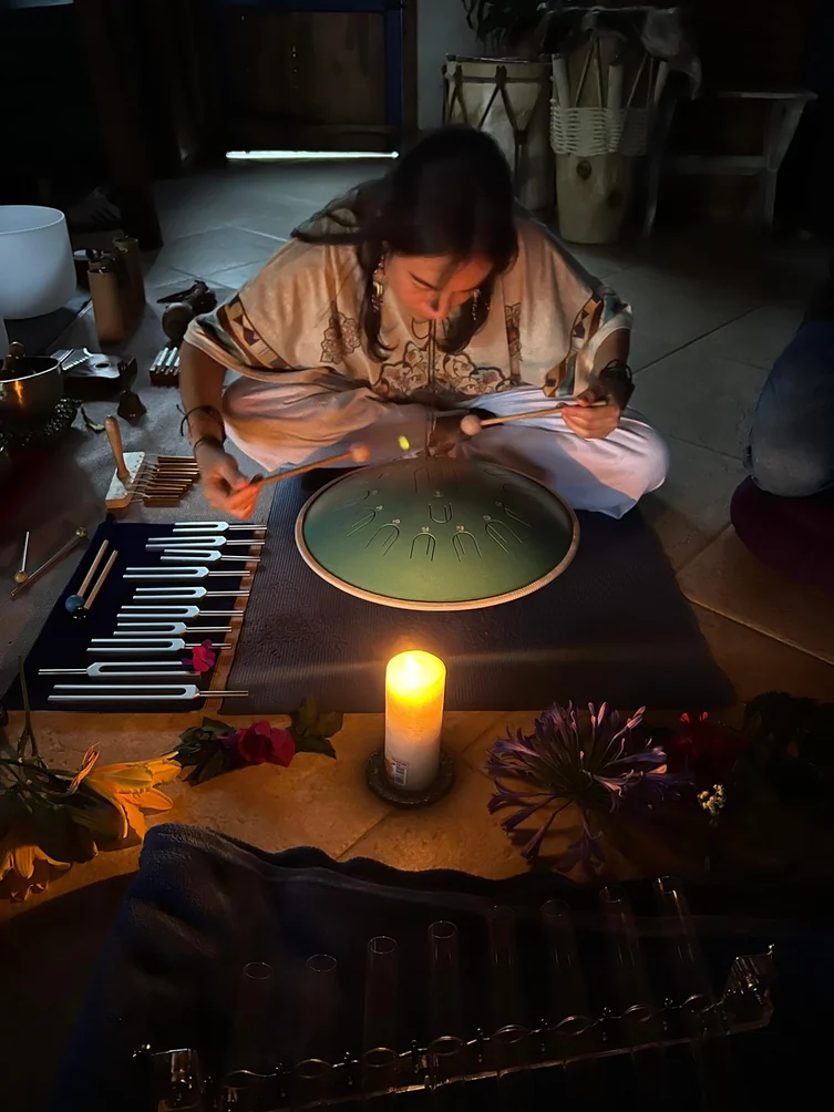 Vanessa playing a tongue drum beside tuning forks and singing bowls at a sound healing ceremony in Medellin