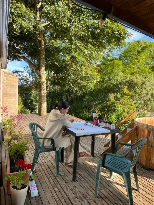 A guest writing at a table on the sunny deck at Harmonica Retreat, surrounded by trees